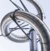 Close-up of large, intertwined, shiny metal pipes against a light sky, showcasing complex industrial engineering