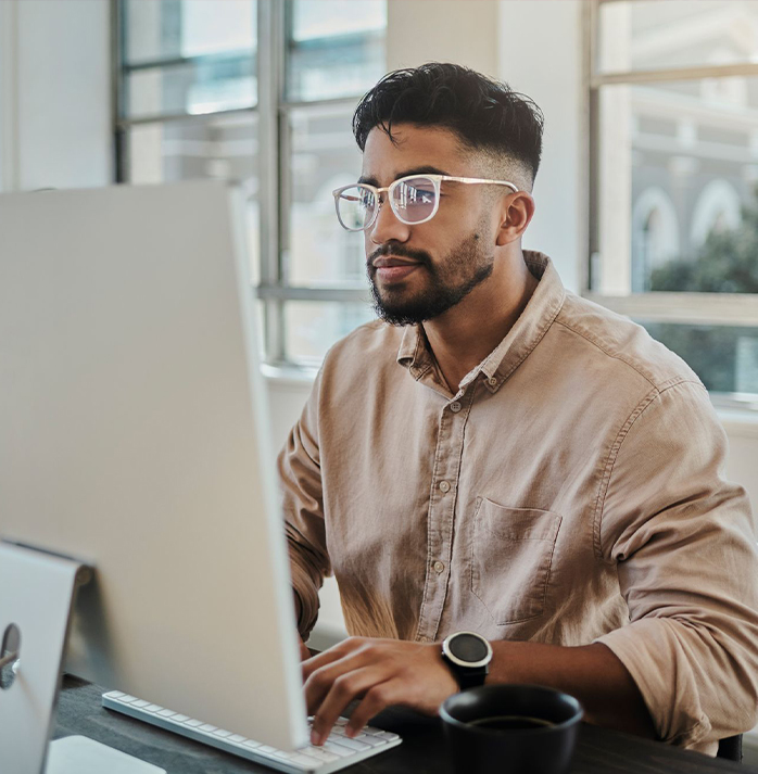 a man with glasses working on a computer in an office enviroment