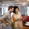 Two colleagues standing in an office, smiling and looking at a laptop together
